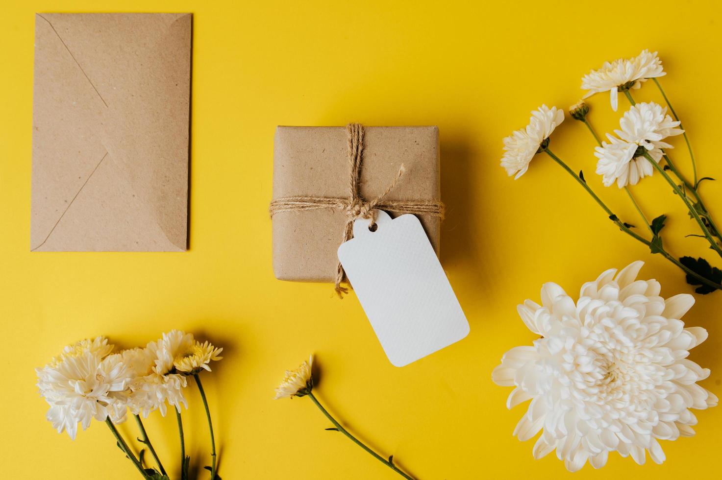geschenkdoos met blanco tag, envelop en bloemen wordt op geel geplaatst foto