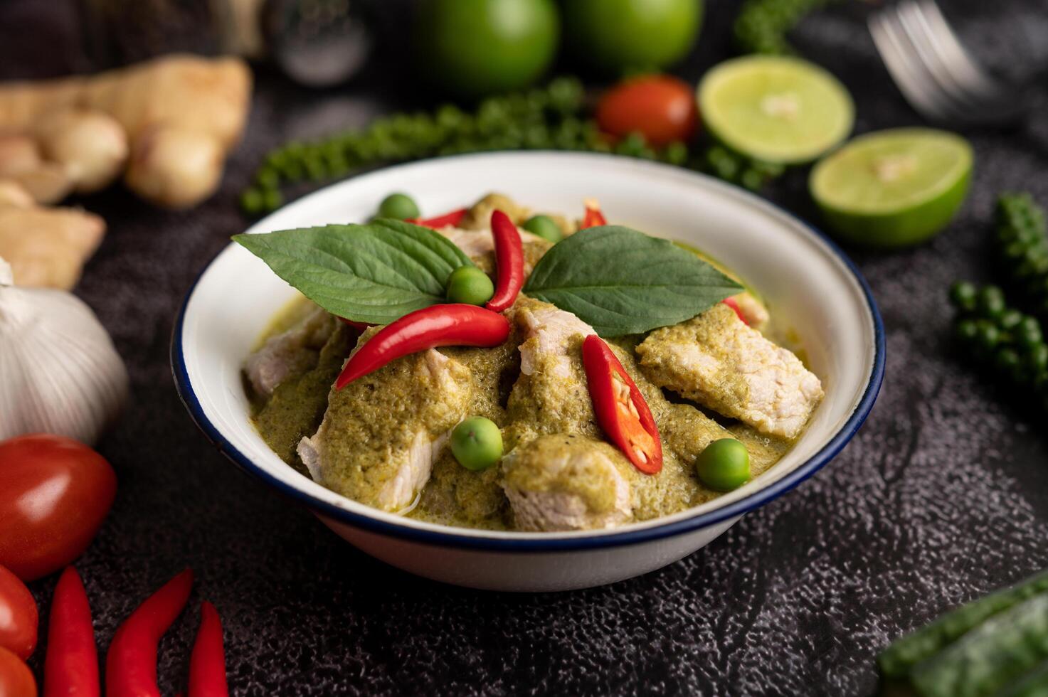 varkensvlees groene curry in een witte kom met kruiden op een zwarte cement foto