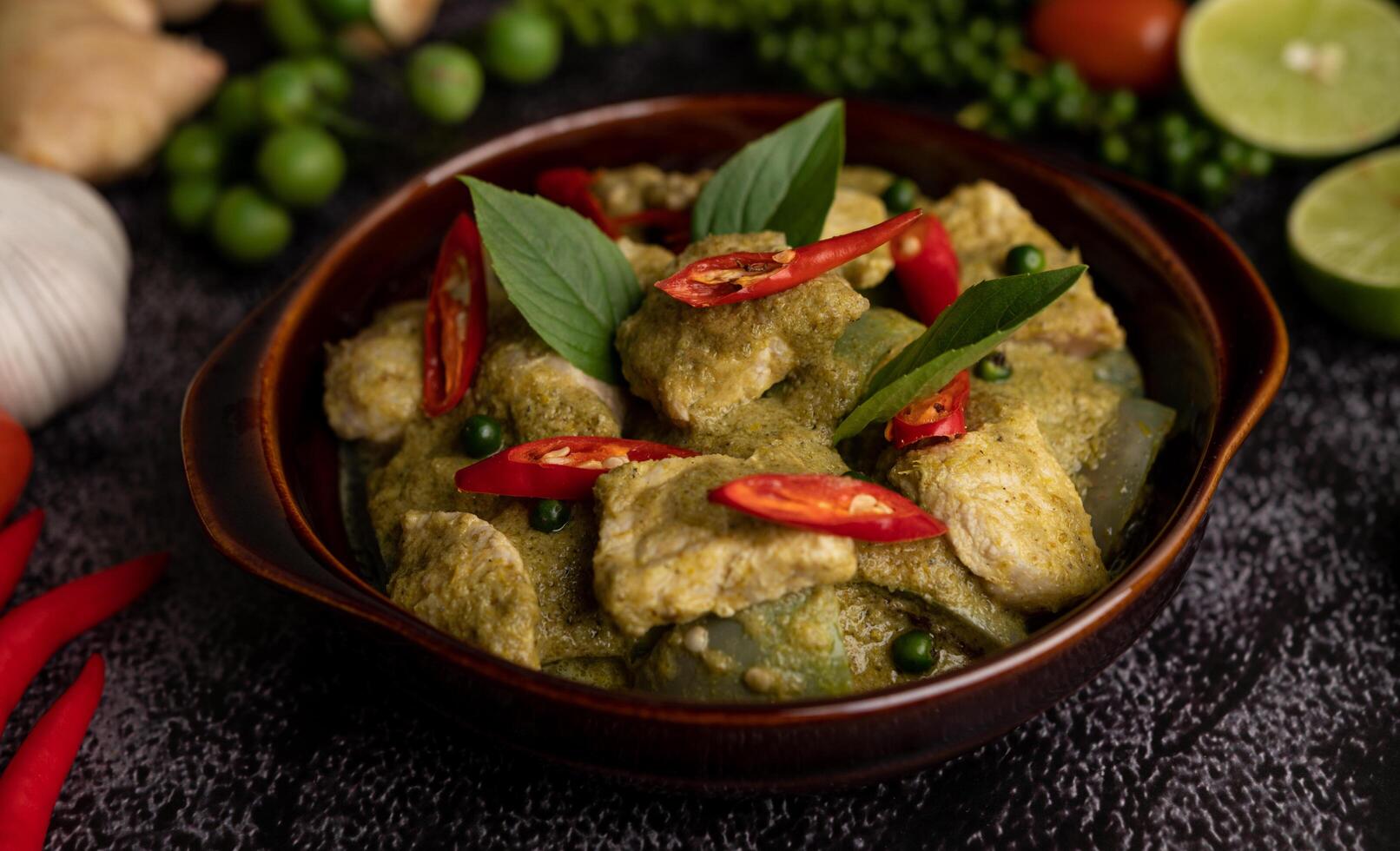 varkensvlees groene curry in een bruine kom met kruiden op een zwarte cement foto