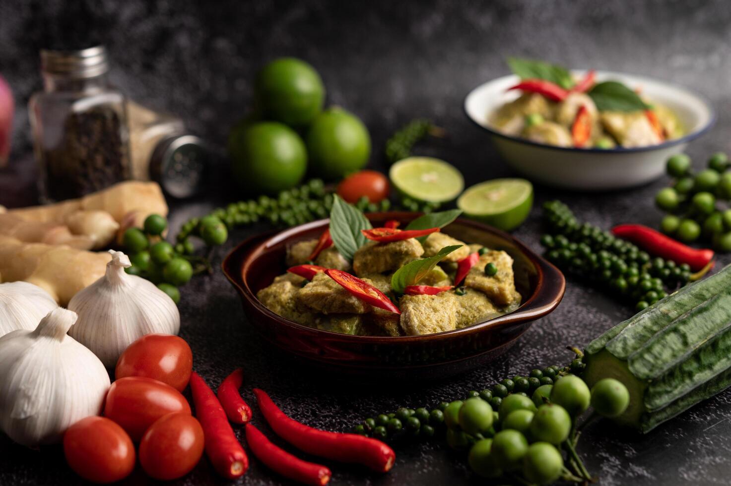 varkensvlees groene curry in een bruine kom met kruiden op een zwarte cement foto