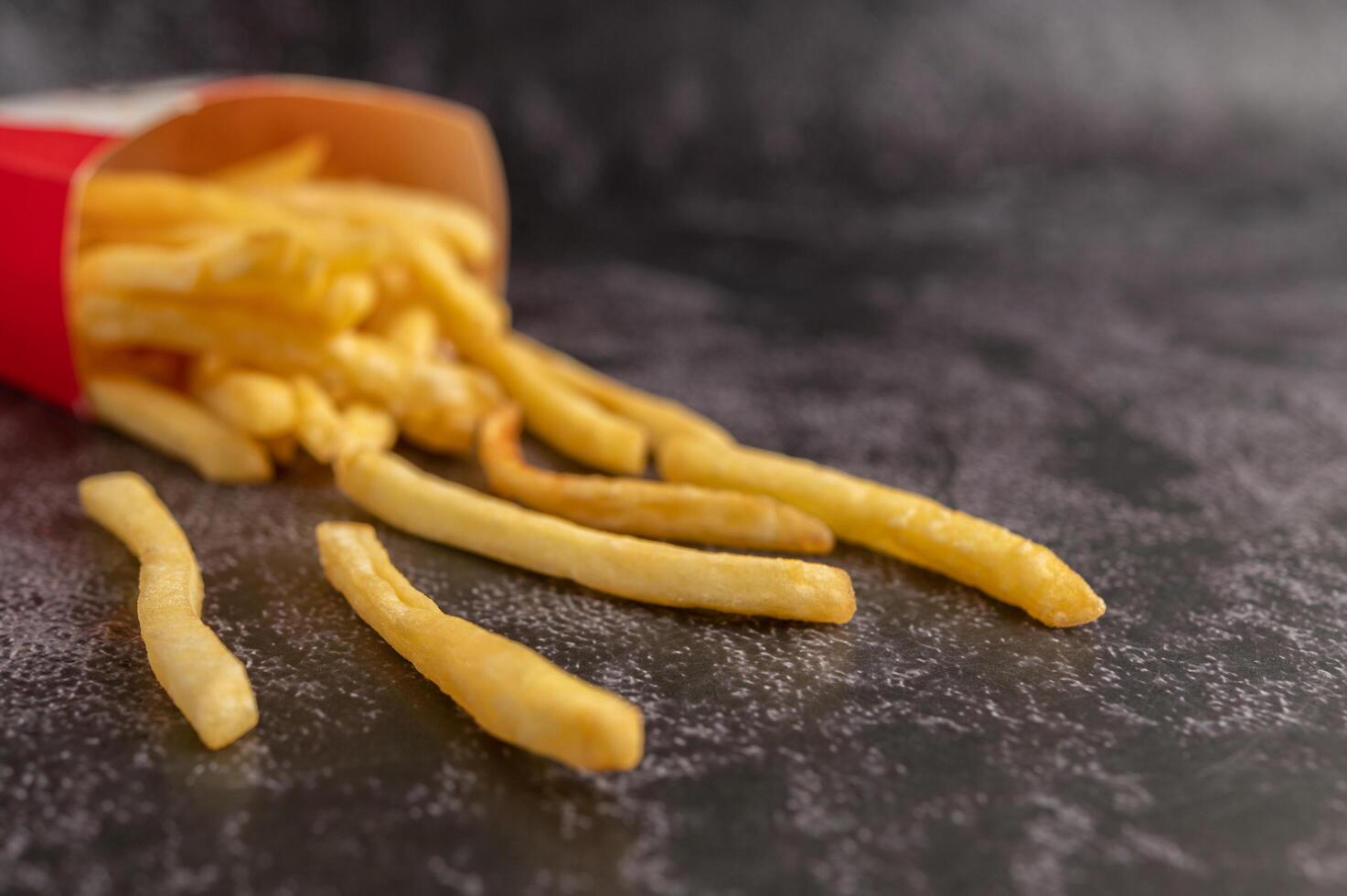 Franse frietjes gegoten uit een zak op een zwarte cementvloer. foto