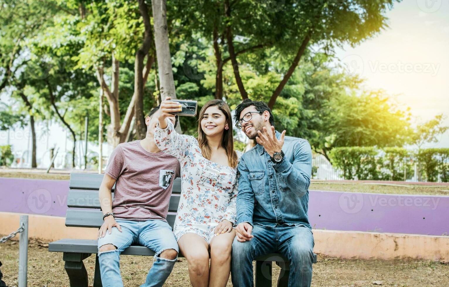 drie vrienden zittend Aan een bank nemen een selfie, drie tiener- vrienden zittend Aan een bank nemen selfies. bijeenkomst van drie gelukkig vrienden nemen een selfie zittend Aan een bank foto