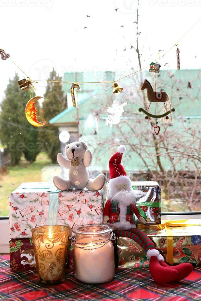 speelgoed- gnoom met teddy beer zittend Aan Kerstmis cadeaus met kaarsen in glas kandelaars in de buurt de venster in een landelijk huis, verticaal foto