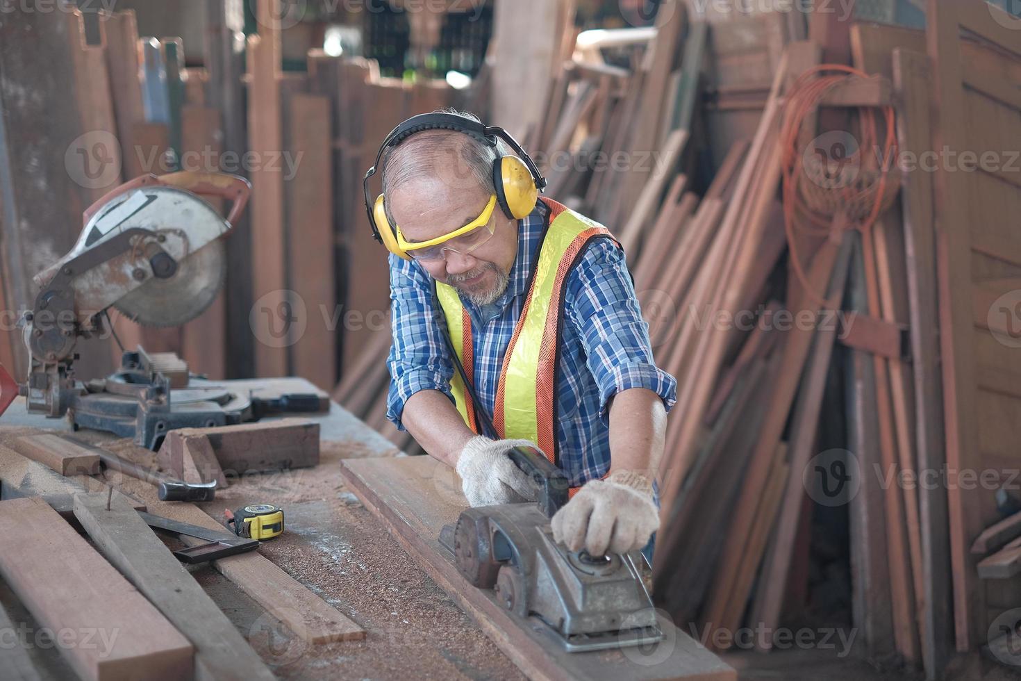 een oude Aziatische mannelijke timmerman werkt in een houtfabriek. foto