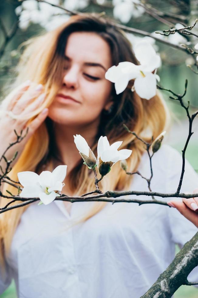 wazig beeld van mooi meisje dat geniet van magnoliabloemen, ogen dicht foto