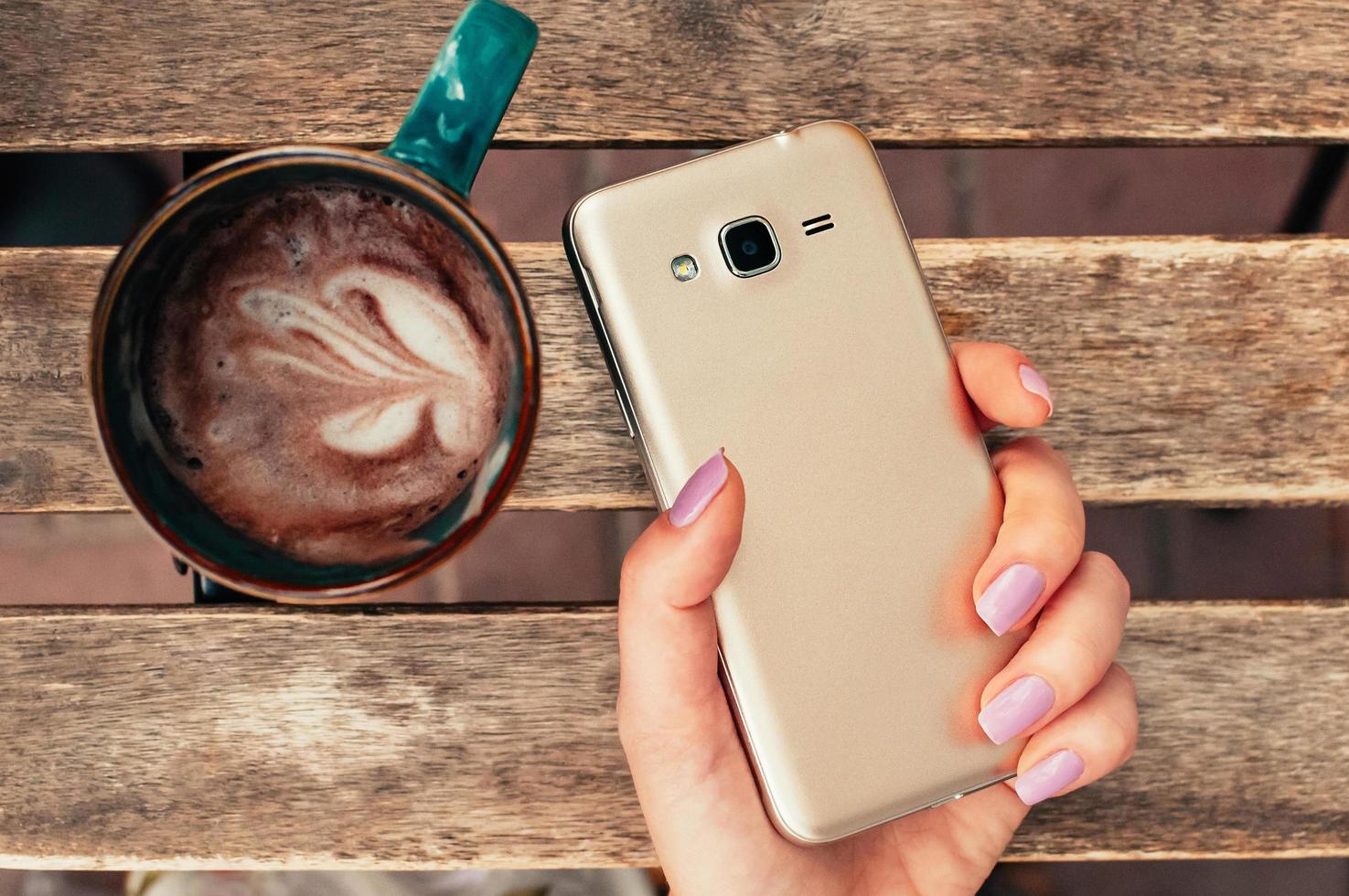 vrouwelijke hand met slimme telefoon in café, met cappuccino op tafel foto