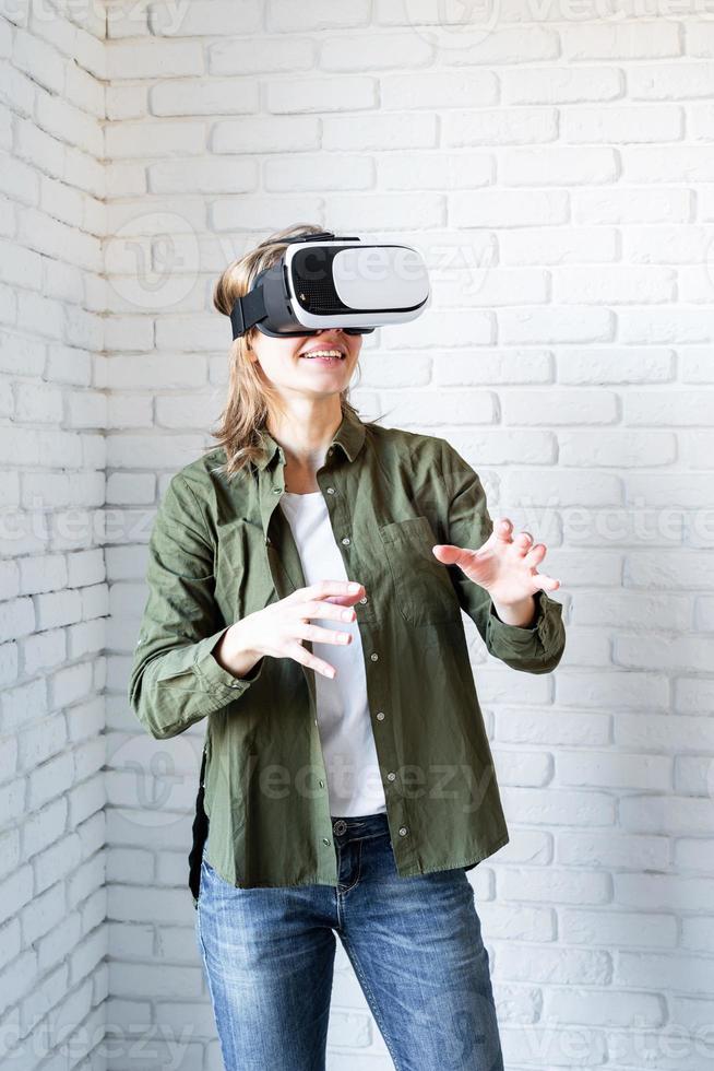 verbaasde vrouw in vr-bril die zich op witte bakstenen muurachtergrond bevindt foto