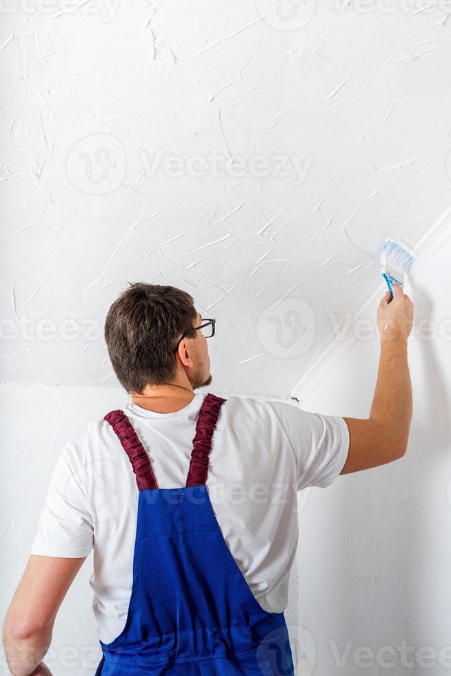 man in blauwe overall schilderen muur met penseel foto