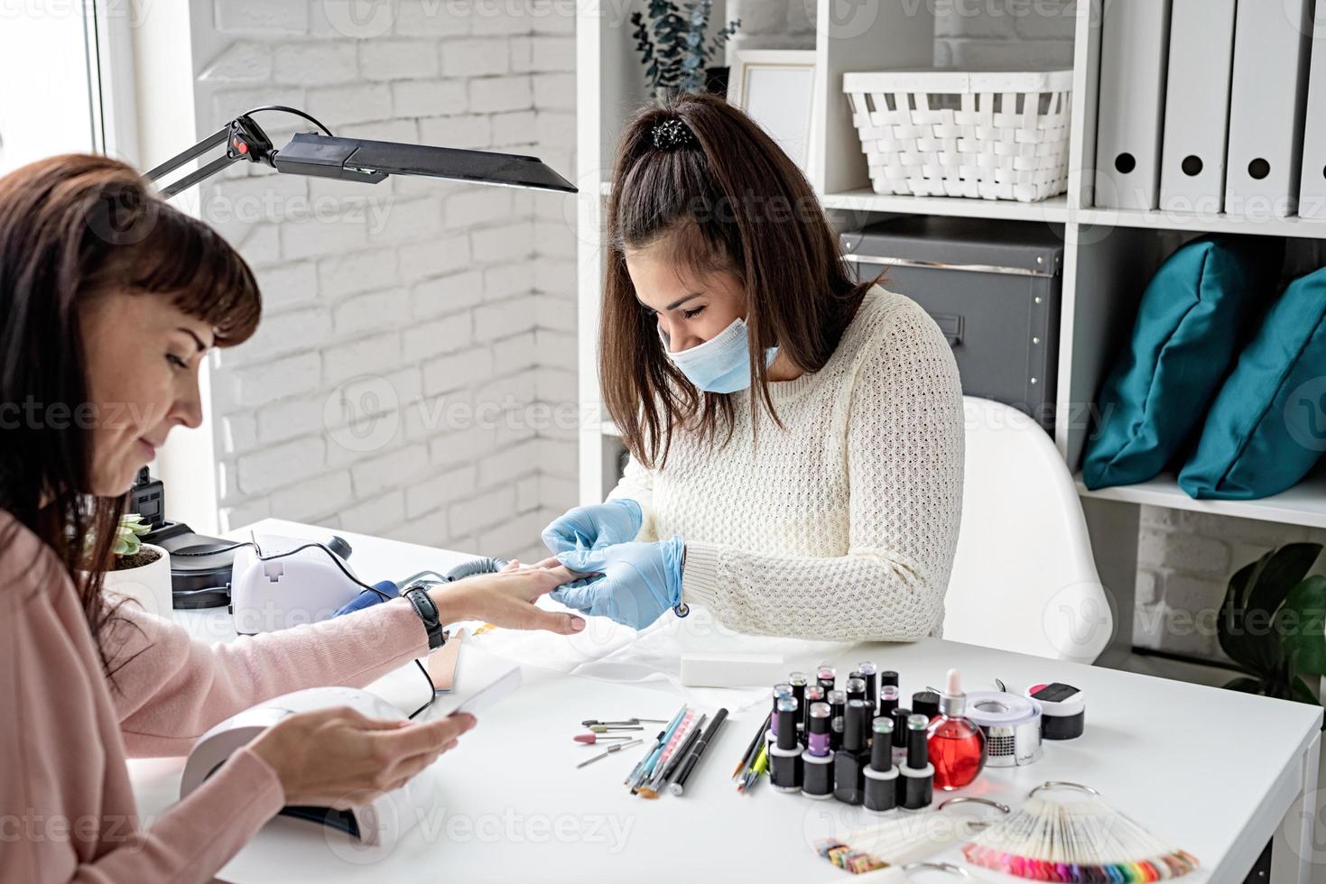 manicure meester in masker en handschoenen die gellak aantrekken foto