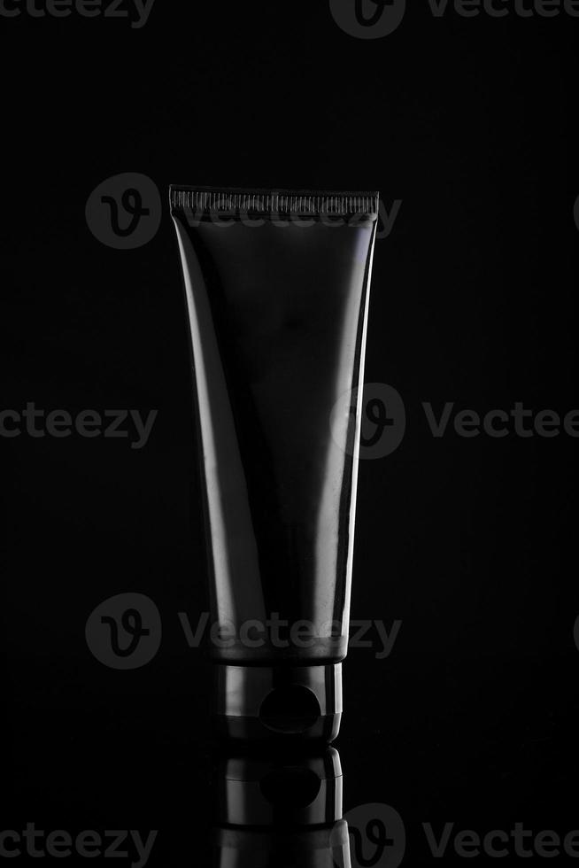 glanzend zwart product cosmetische buis op zwarte achtergrond foto