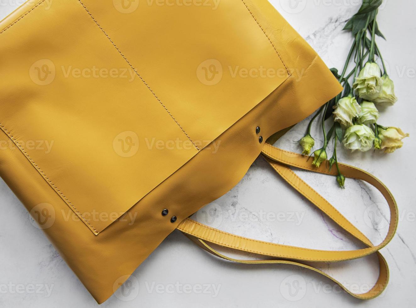 grote gele leren tas en bloemen op marmeren achtergrond foto