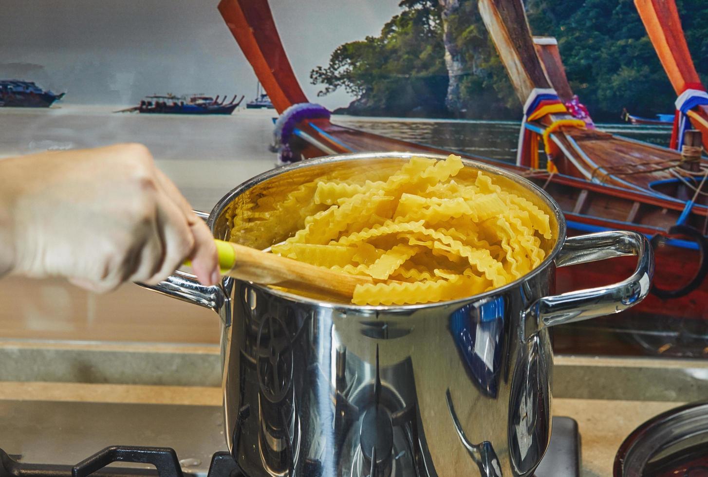 vrouw roert kokende mafaldine - vorm van spaghetti in pan foto