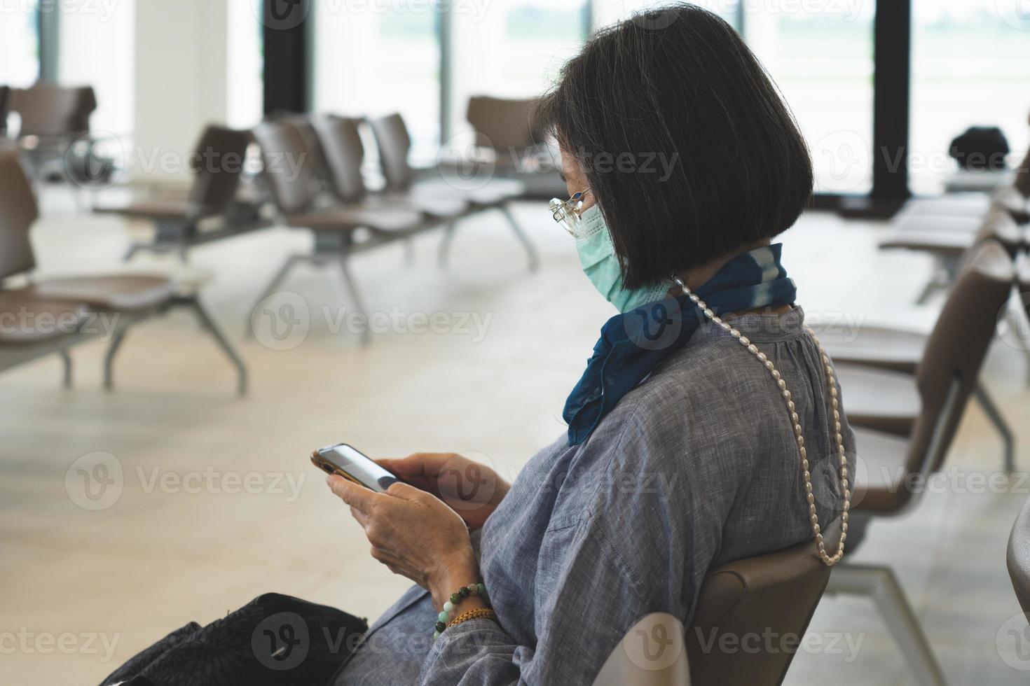 senior aziatische vrouw die een masker draagt terwijl ze op de luchthaven zit foto