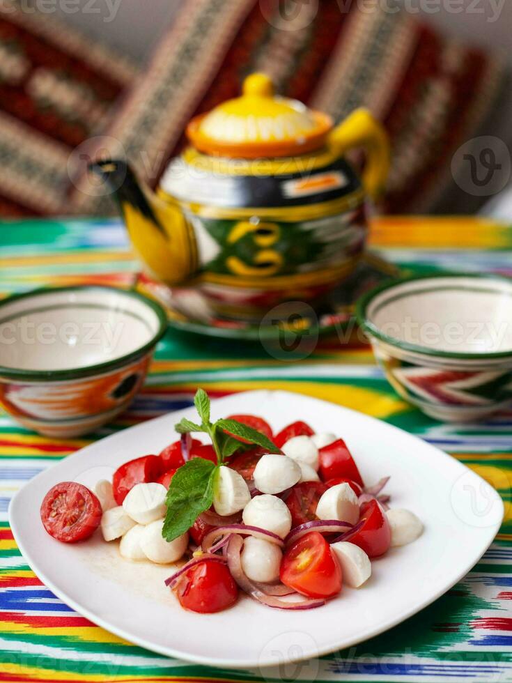 caprese salade met Mazzarella tomaten en kruiden in oosters stijl Aan een tafel met een theepot en een kop voor thee. foto