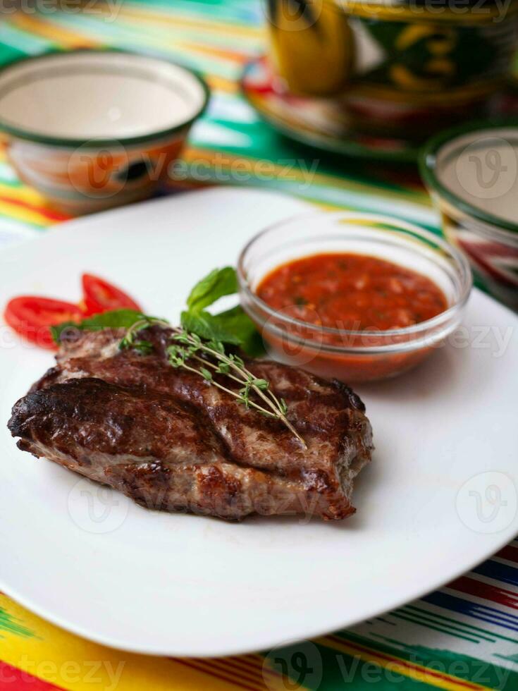 rundvlees steak met tomaat saus, tomaten en kruiden in oosters stijl Aan een tafel met een theepot en een kop voor thee. foto
