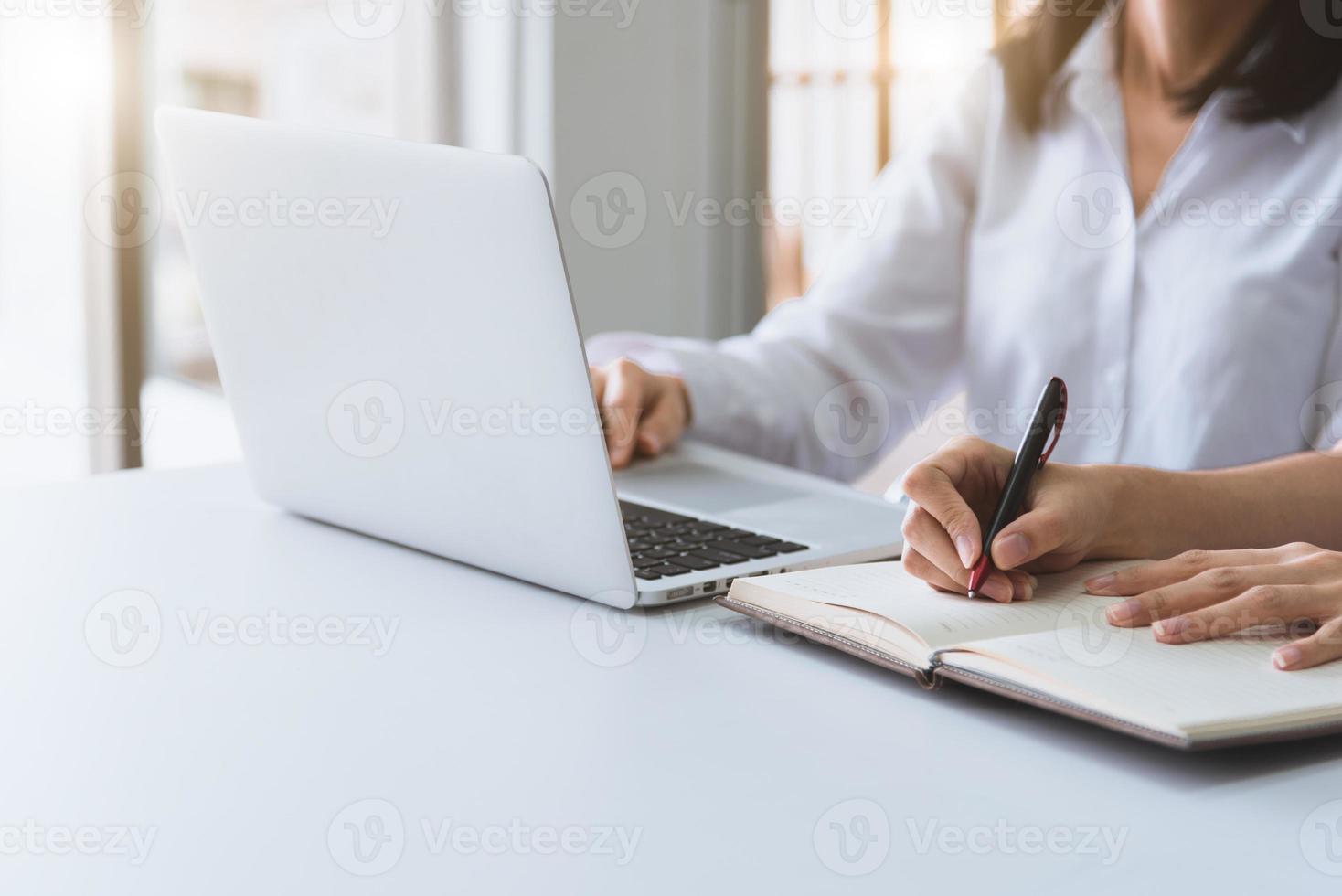 close-up van twee zakenvrouwen die een laptop gebruiken en op een notebook schrijven foto