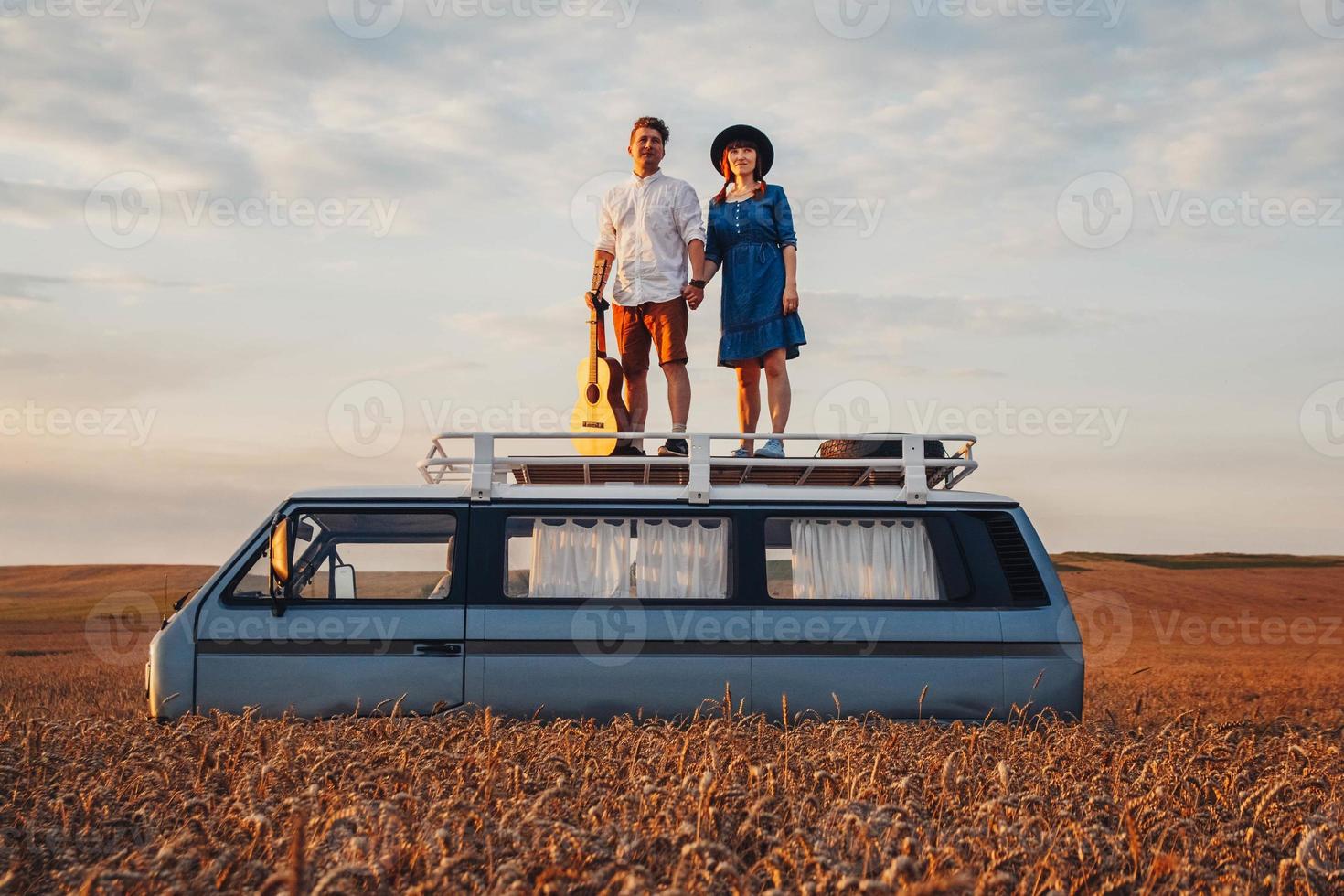 man met gitaar en vrouw op het dak van een auto in een tarweveld foto