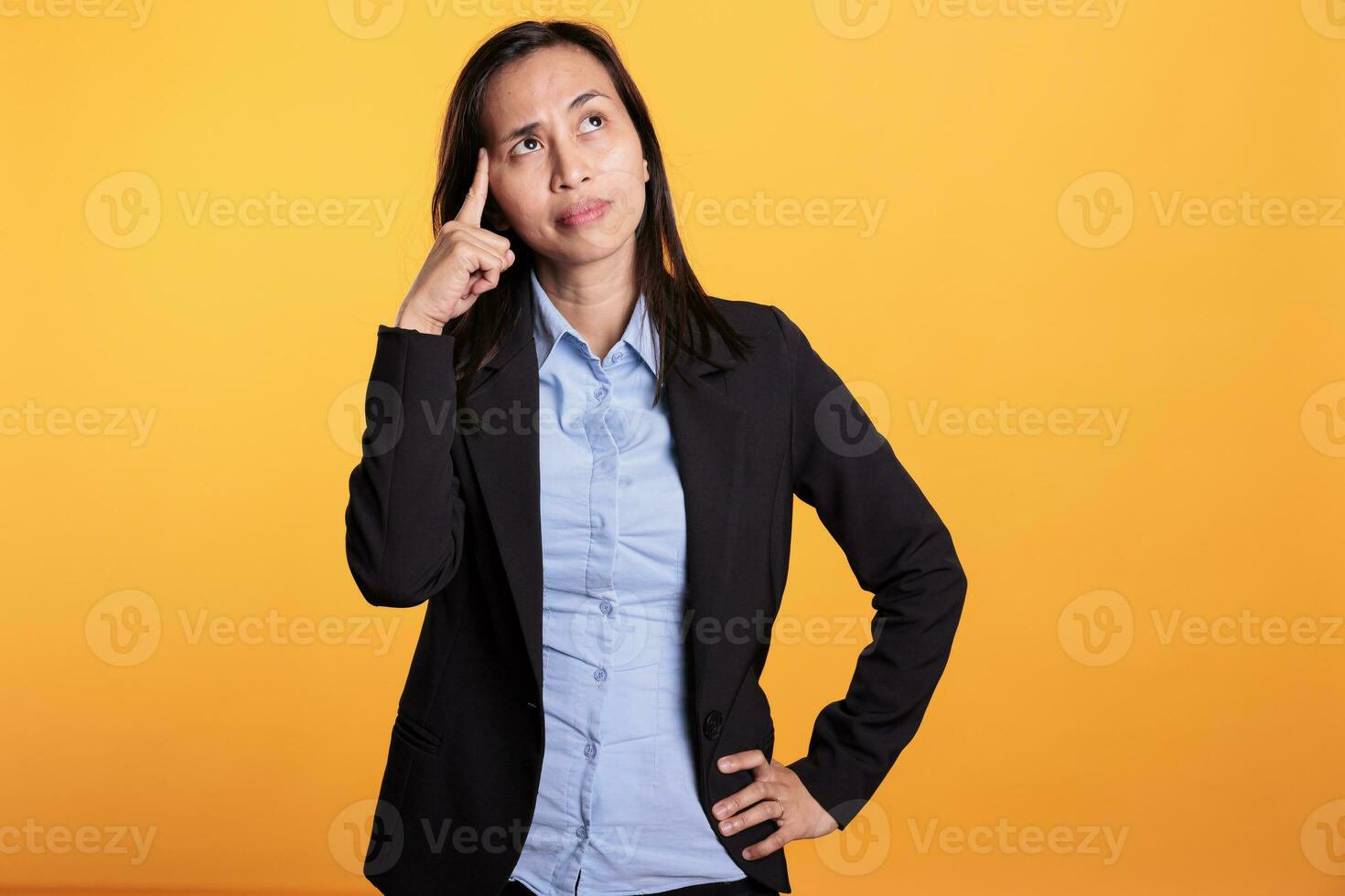 attent Filipijns vrouw Holding vinger Aan tempel brainstorming ideeën, poseren twijfelachtig in studio over- geel achtergrond. nadenkend zakenvrouw in formeel pak overweegt over echt probleem foto