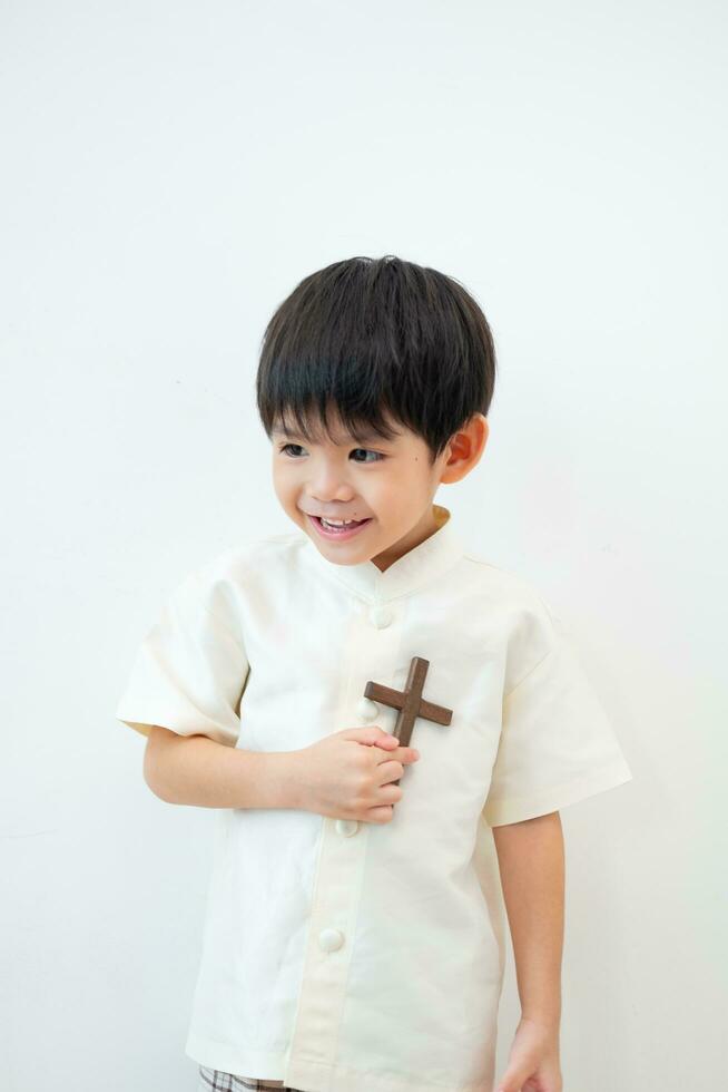 weinig Aziatisch jongen bidden met Holding de kruis, christen concept foto