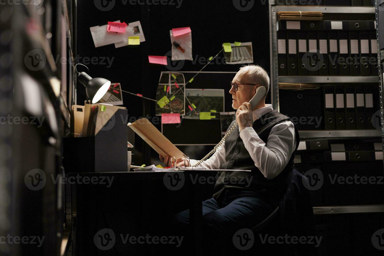 ouderen Politie officier analyseren crimineel geval bestanden bewijs terwijl pratend Bij vaste telefoon telefoon met afgelegen inspecteur. senior privaat detectives werken na een tijdje Bij federaal onderzoek in archiveren kamer foto