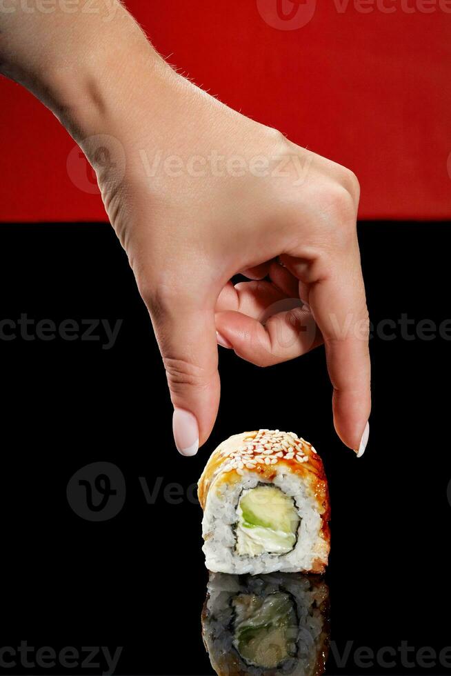 vrouw hand- bereiken uit naar unagi rollen met aal, room kaas en avocado foto