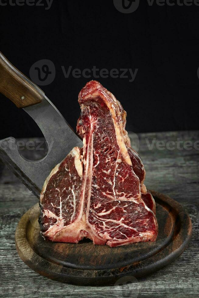 vers rauw t-bones steak Aan een olijf- houten bord met zee zout en een keuken bijl. foto