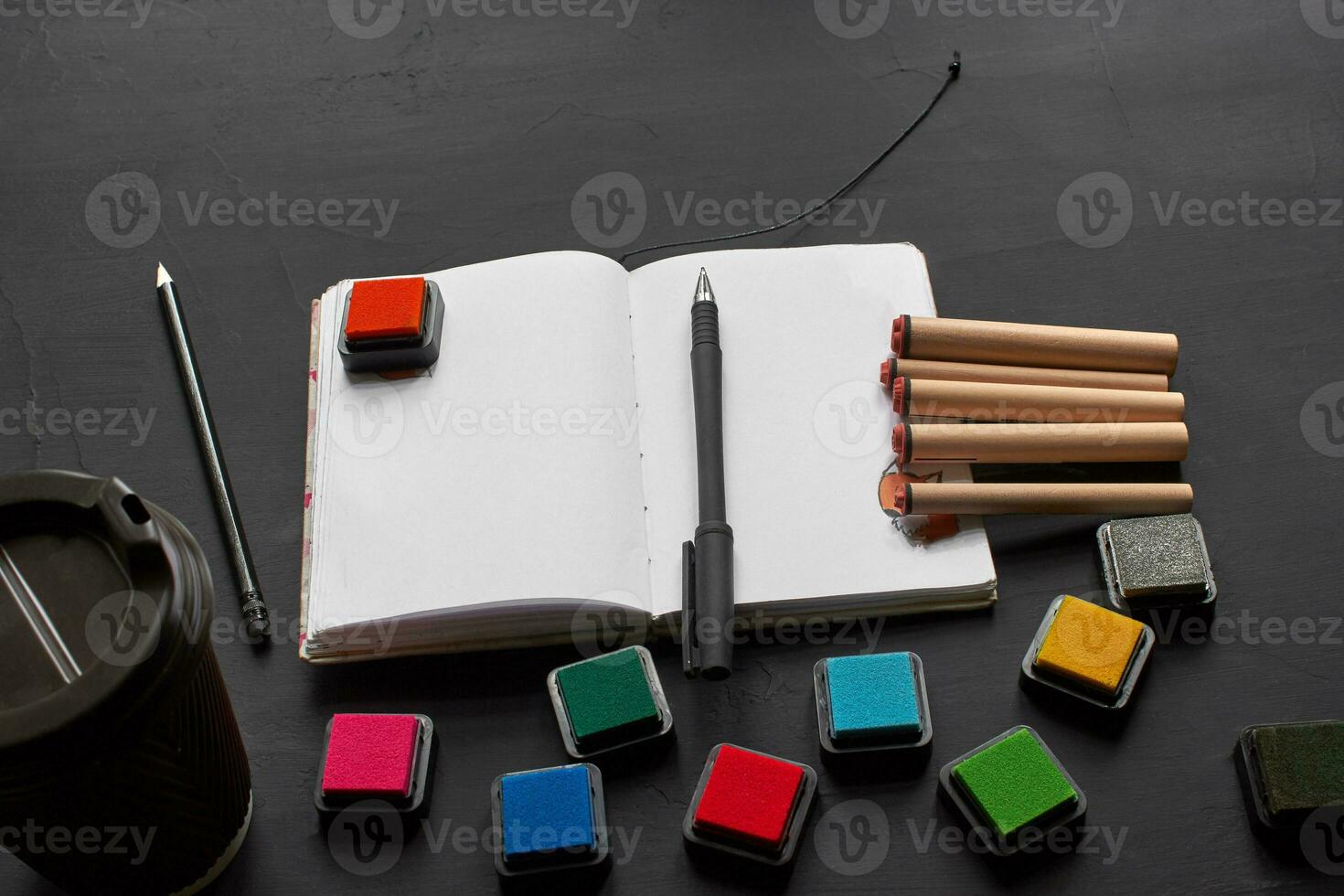 top visie van een leeg notitieboekje, plakboek accessoires en een kop van koffie Aan een zwart achtergrond. foto
