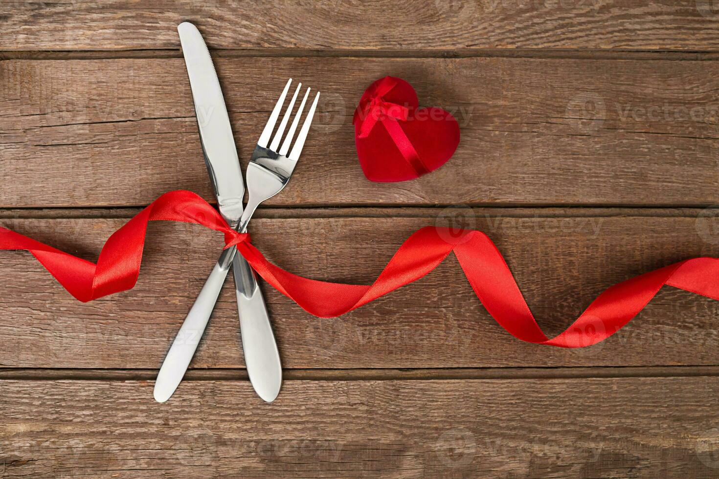 Valentijnsdag dag avondeten tafel instelling met rood lint, mes en vork ring over- eik achtergrond. foto