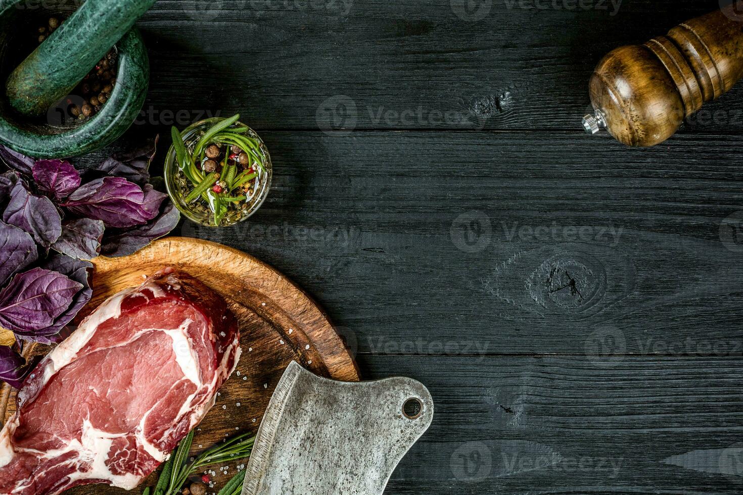 vers rauw rundvlees met basilicum en een takje van rozemarijn met bijl voor vlees Aan zwart houten achtergrond. top visie foto
