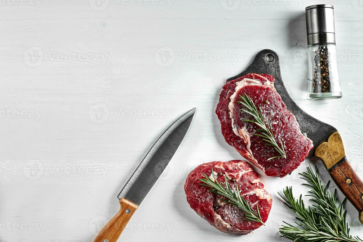 twee vers rauw steaks met kruiden, knoflook, olijf- olie, peper, zout, rozemarijn en een keuken bijl Aan wit achtergrond. top visie. foto