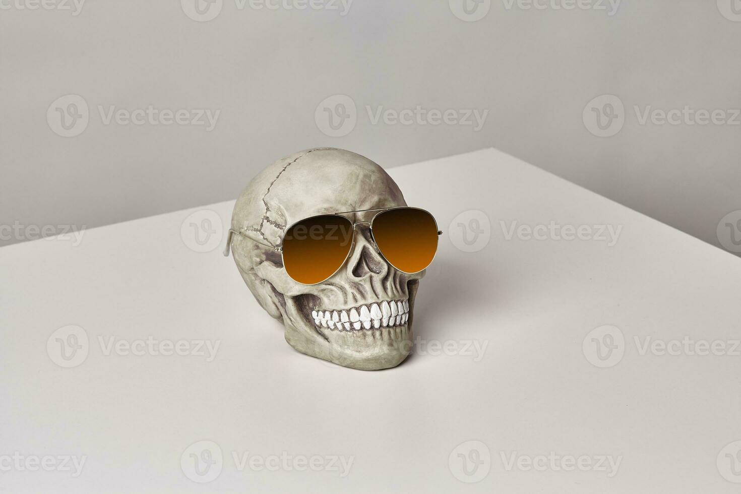 realistisch model- van een menselijk schedel met tanden in een geel zonnebril Aan een licht tafel, wit achtergrond. medisch wetenschap of halloween verschrikking concept. foto