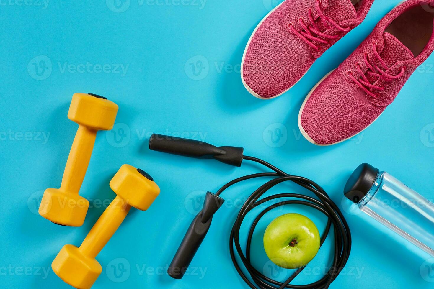 vlak leggen van vrouw sport apparatuur, springen touw, fles van water en roze sportschoenen Aan blauw achtergrond foto