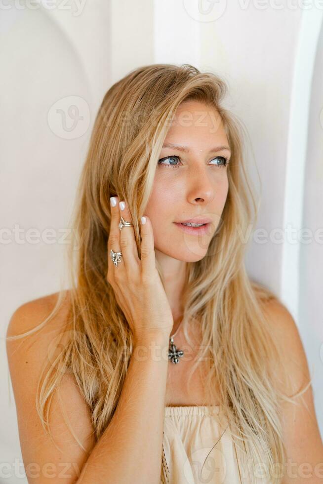 dichtbij omhoog portret van blond vrouw in gewoontjes kleding poseren over- elegant beige interieur. accessoires, tropisch stemming, vakantie tijd. foto