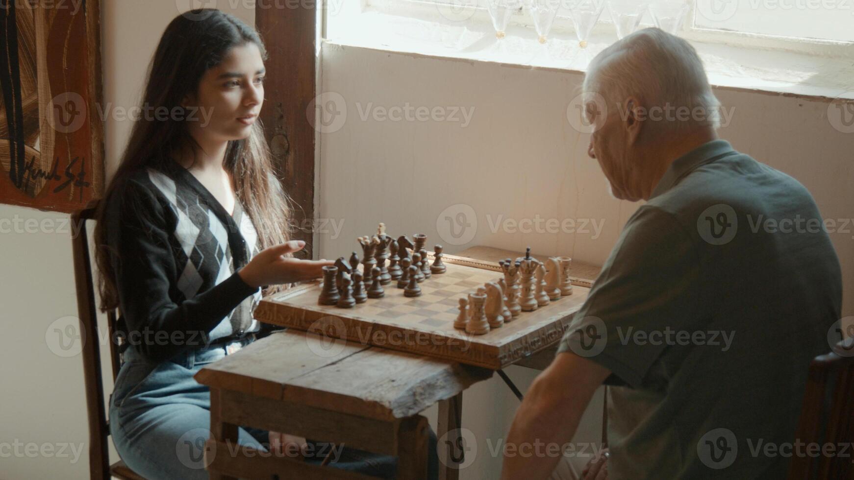 meisje legt uit hoe je moet schaken aan een man die aan tafel zit foto