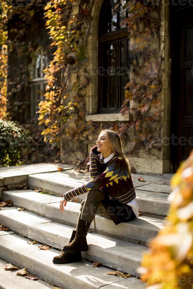jonge vrouw zittend op een trap met mobiele telefoon in herfst park foto