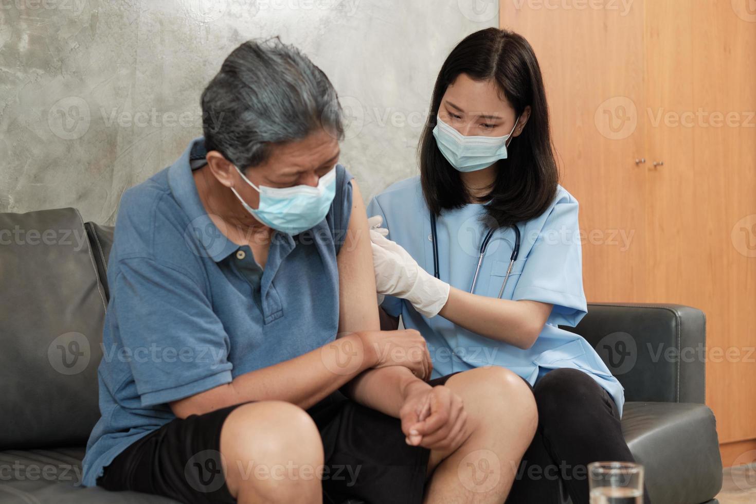 een aziatische vrouwelijke arts vaccineert thuis een oudere man. foto