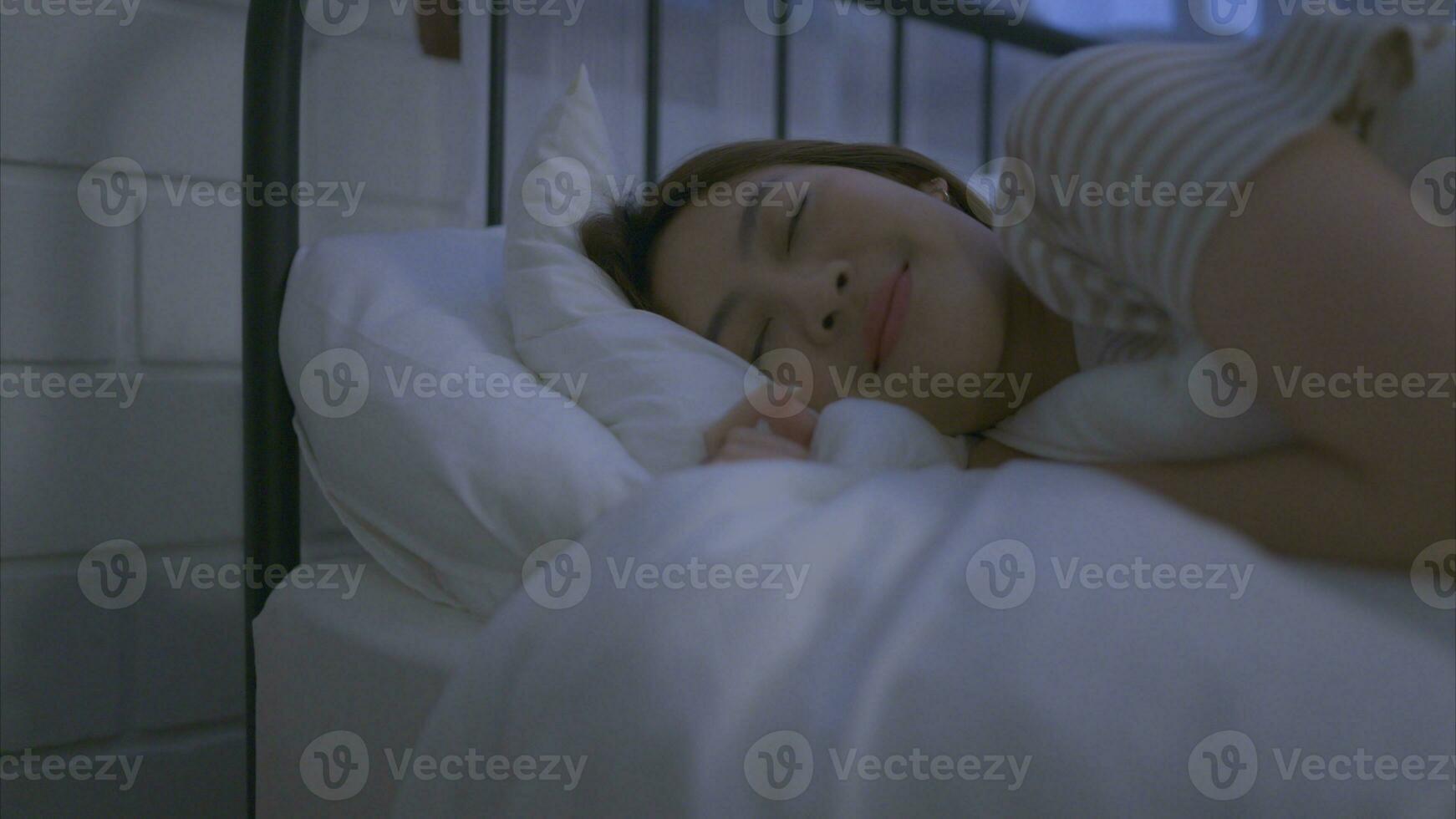 Aziatisch jong vrouw beurt uit de nachtkastje licht en vervolgens haar slaap Aan een zacht hoofdkussen foto