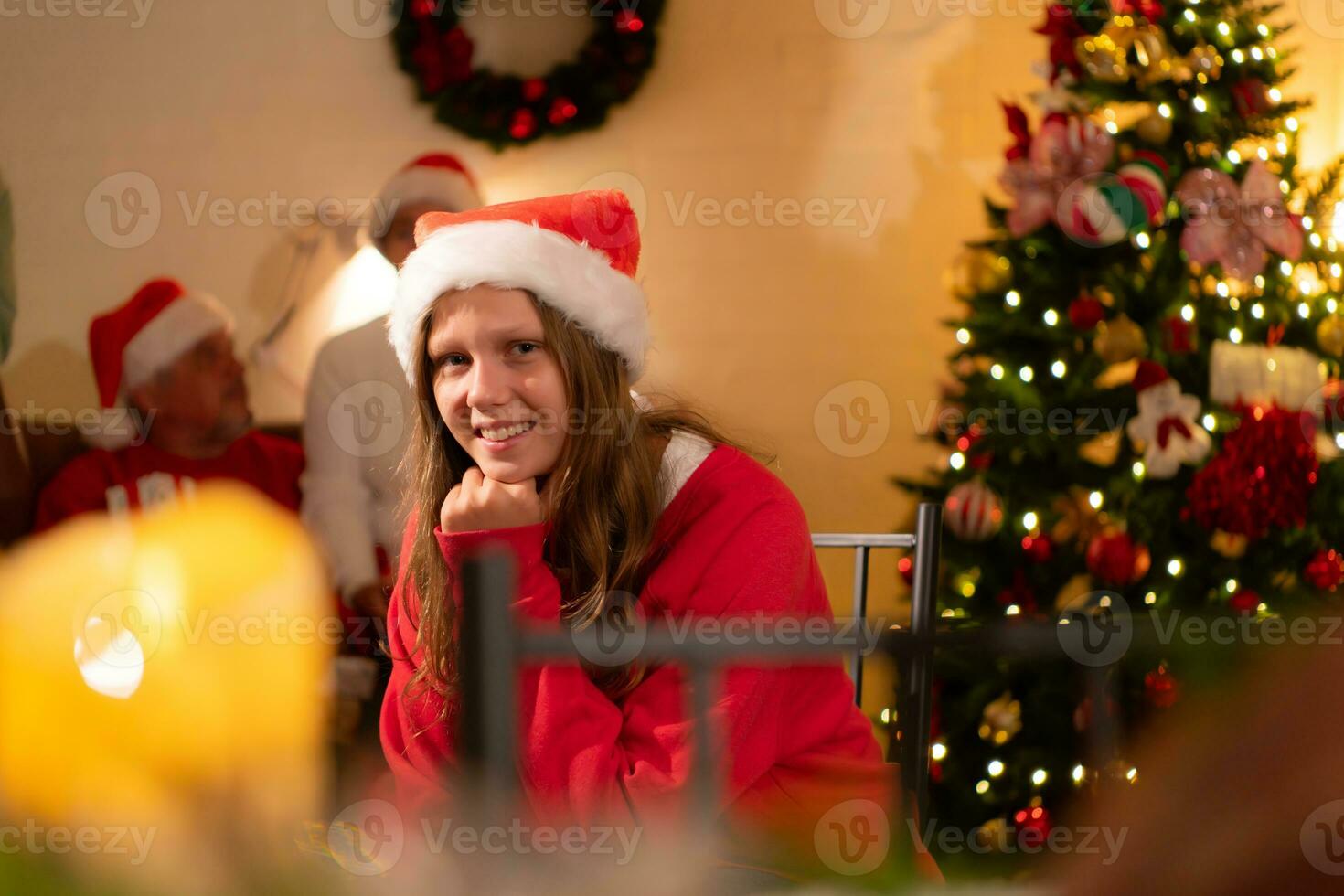 portret van tiener- meisje in de kerstman hoed zittend Aan stoel in voorkant van Kerstmis boom, vrolijk Kerstmis en gelukkig vakantie foto