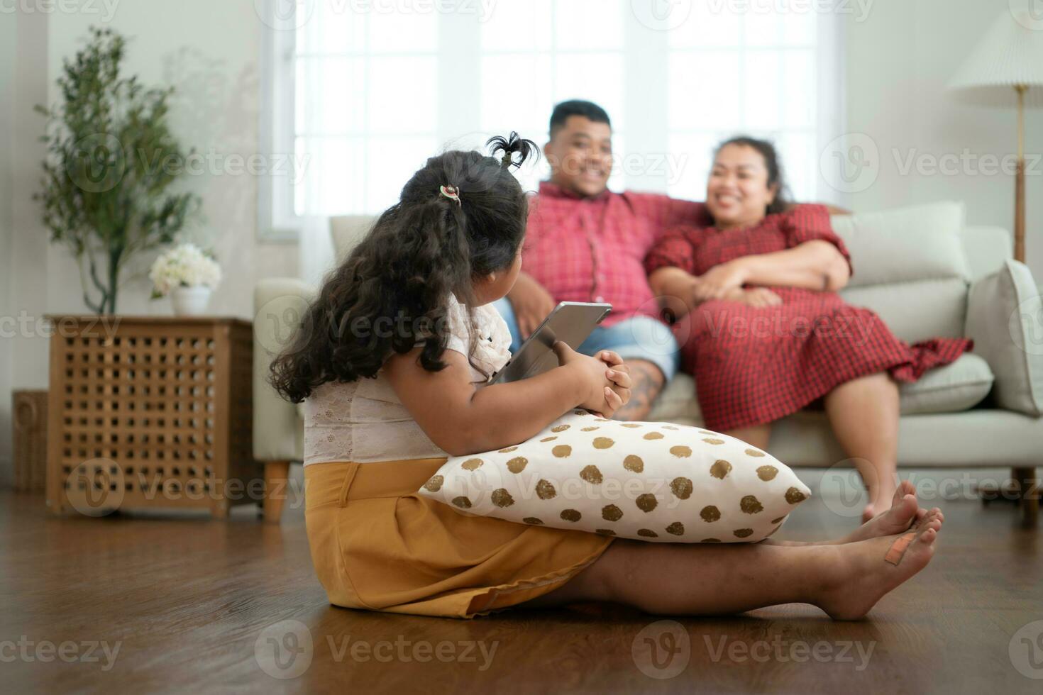 een plus grootte familie met een vader vervelend een prothetisch been, gedurende rust uit tijd toestaan dochter naar Speel spellen Aan tablet in de leven kamer van de huis. foto