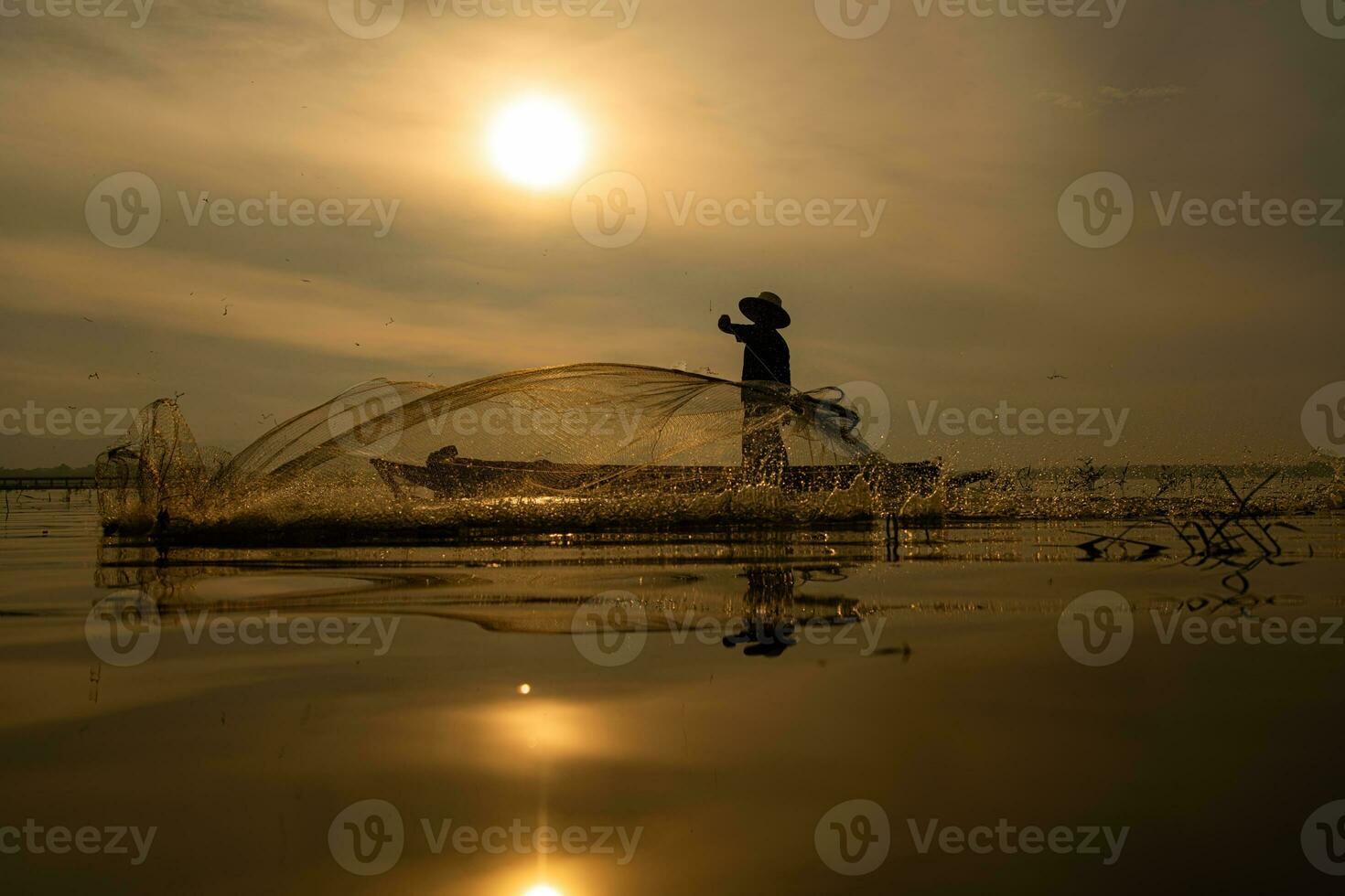 silhouet van visser Bij zonsopkomst, staand aan boord een roeien boot en gieten een netto naar vangst vis voor voedsel foto