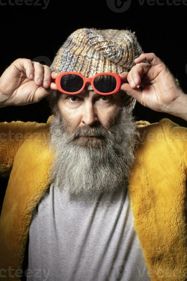 verticaal portret van een ouderen Mens vervelend modieus kleren en rood bril. foto