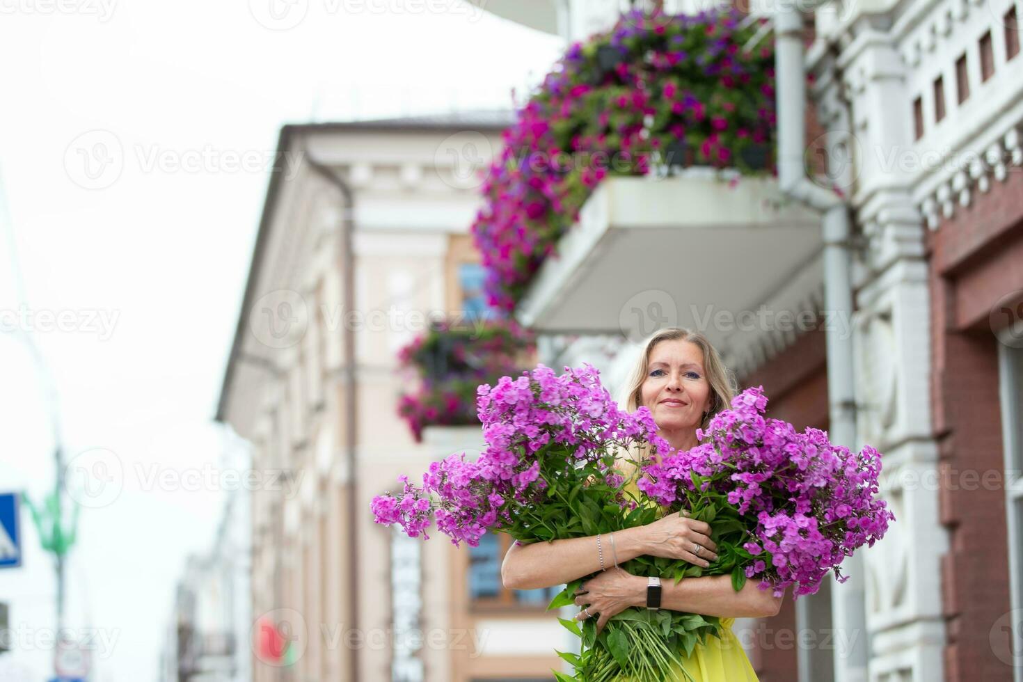 een mooi ouderen vrouw met een boeket van bloemen wandelingen in de omgeving van de stad. leeftijd model- blond met blauw ogen is gelukkig. een vrouw van vijftig jaren wandelingen in de zomer, hebben een mooi zo tijd. foto