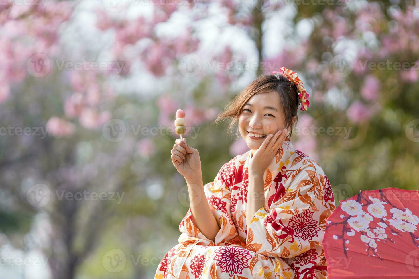 Japans vrouw in traditioneel kimono jurk Holding zoet Hanami dango toetje terwijl wandelen in de park Bij kers bloesem boom gedurende voorjaar sakura festival foto