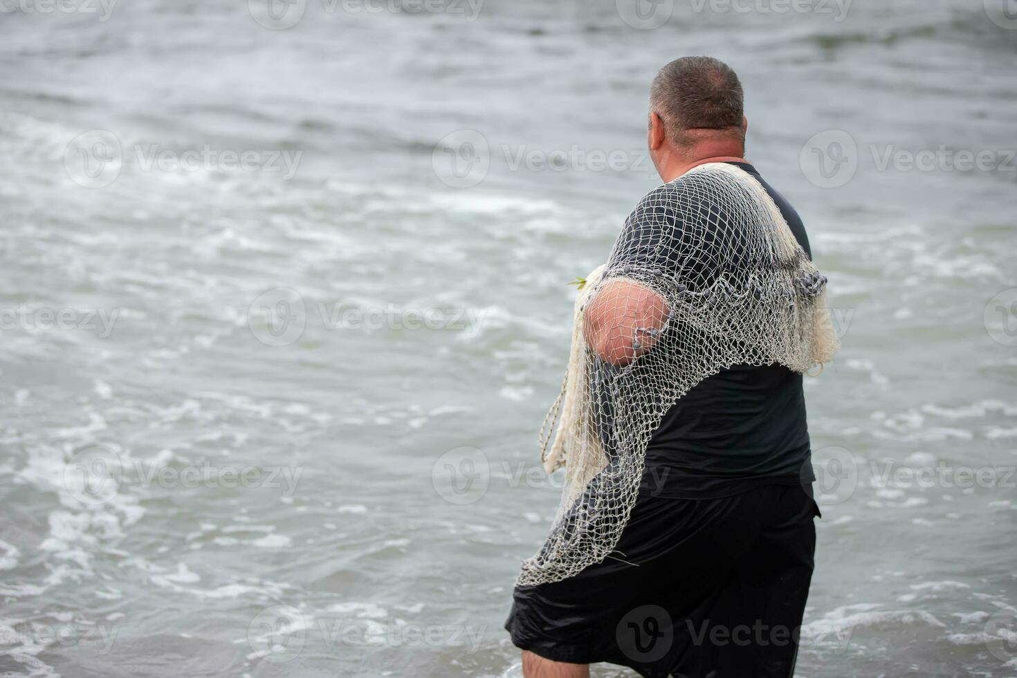 een visser met een visvangst netto komt binnen de zee. foto