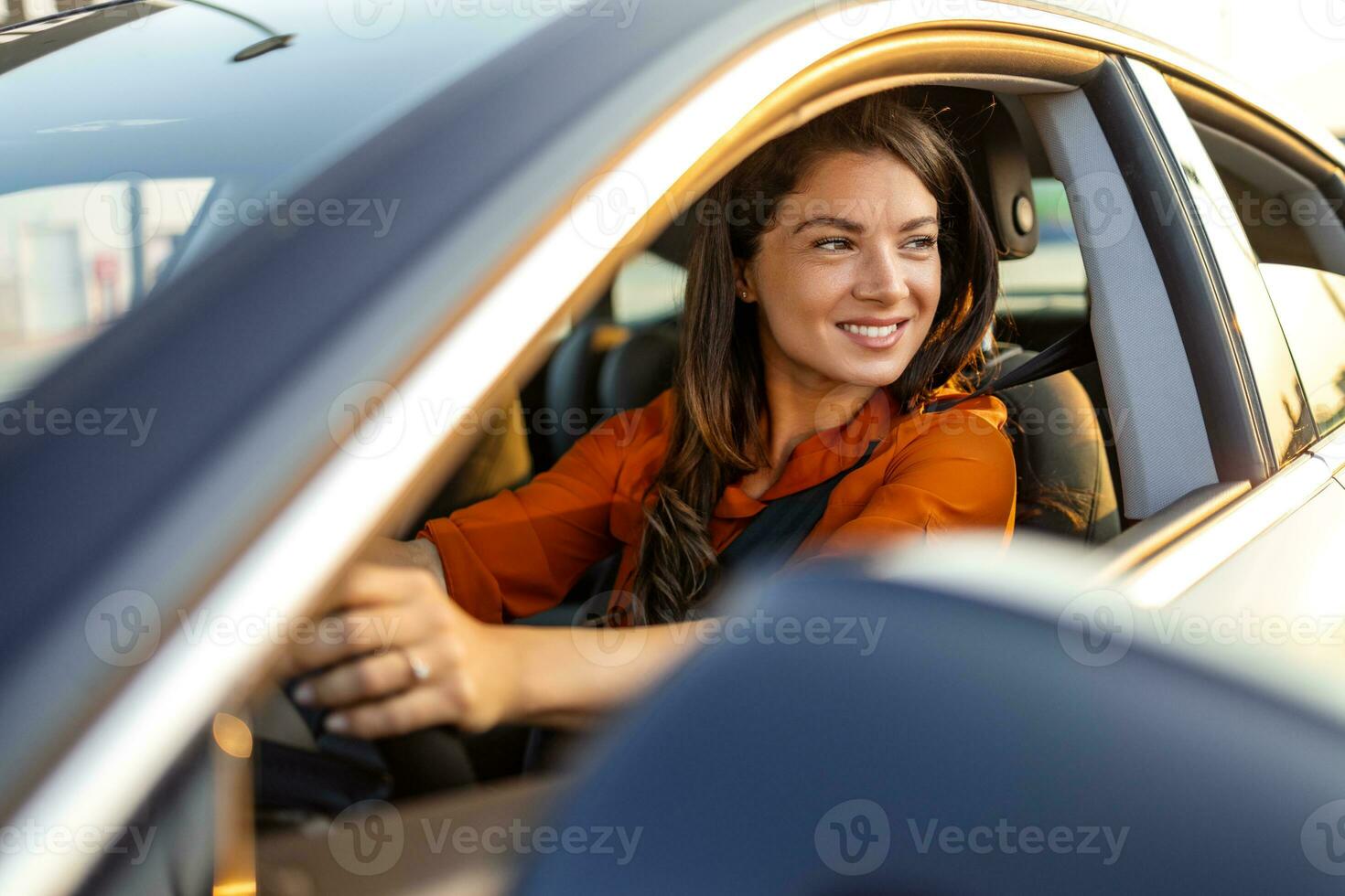 mooi jong gelukkig glimlachen vrouw het rijden haar nieuw auto Bij zonsondergang. portret van glimlachen jong Kaukasisch vrouw zittend alleen Aan bestuurder stoel met vastmaken riem terwijl het rijden modern auto. foto