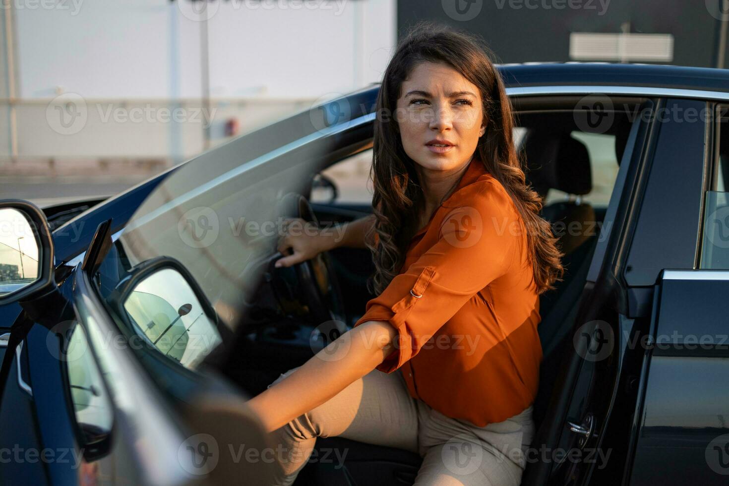 jong vrouw krijgen uit van een modern met auto met natuurlijk zonnig licht. portret van aantrekkelijk en gelukkig bedrijf vrouw krijgen uit van haar modern auto en lachend. gaan naar de kantoor foto