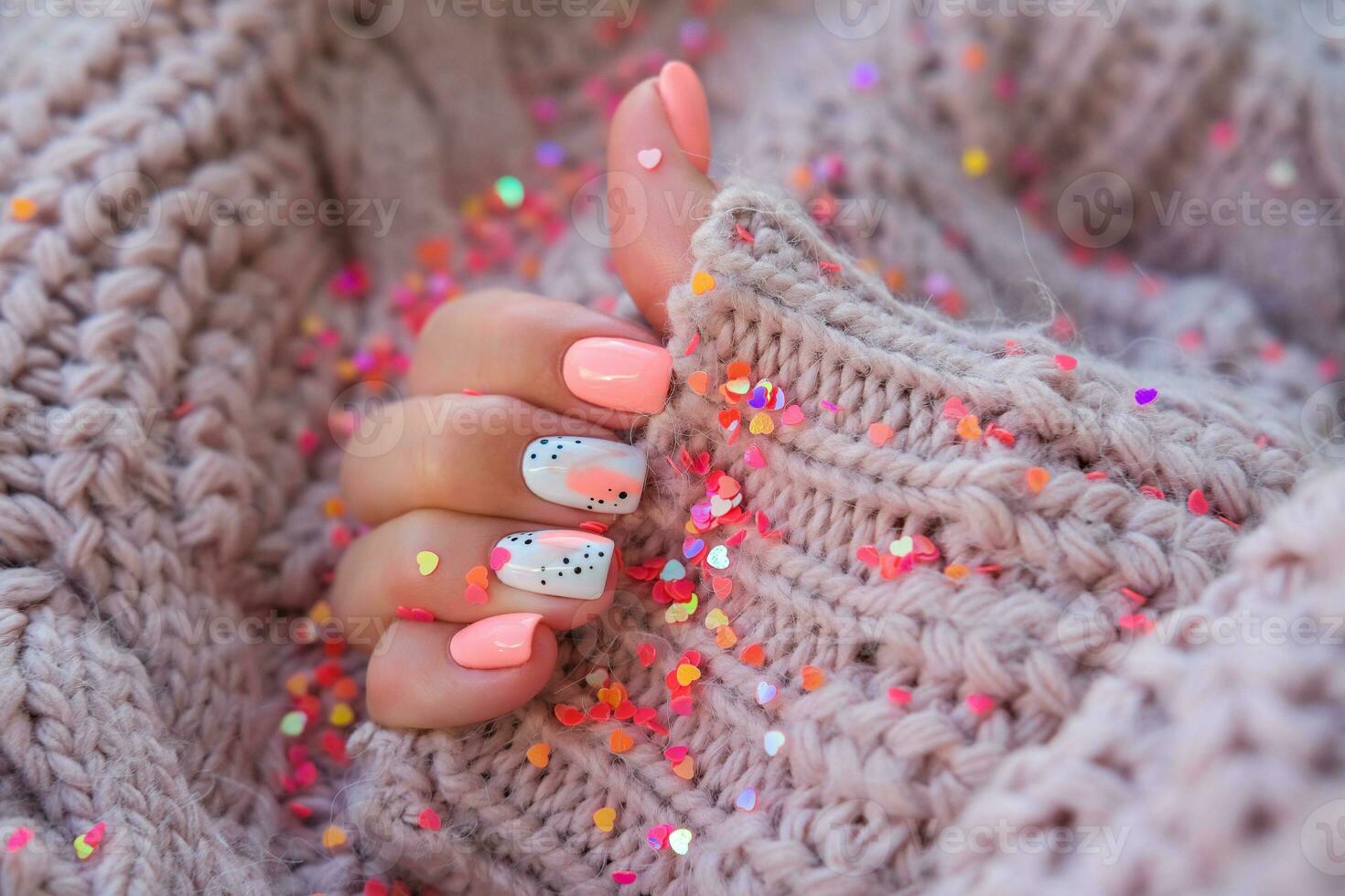 vrouwen handen met een mooi roze manicure in een warm gebreid trui en hartvormig pailletten. winter tendens, Hoes roze nagels met gel Pools, schellak. foto