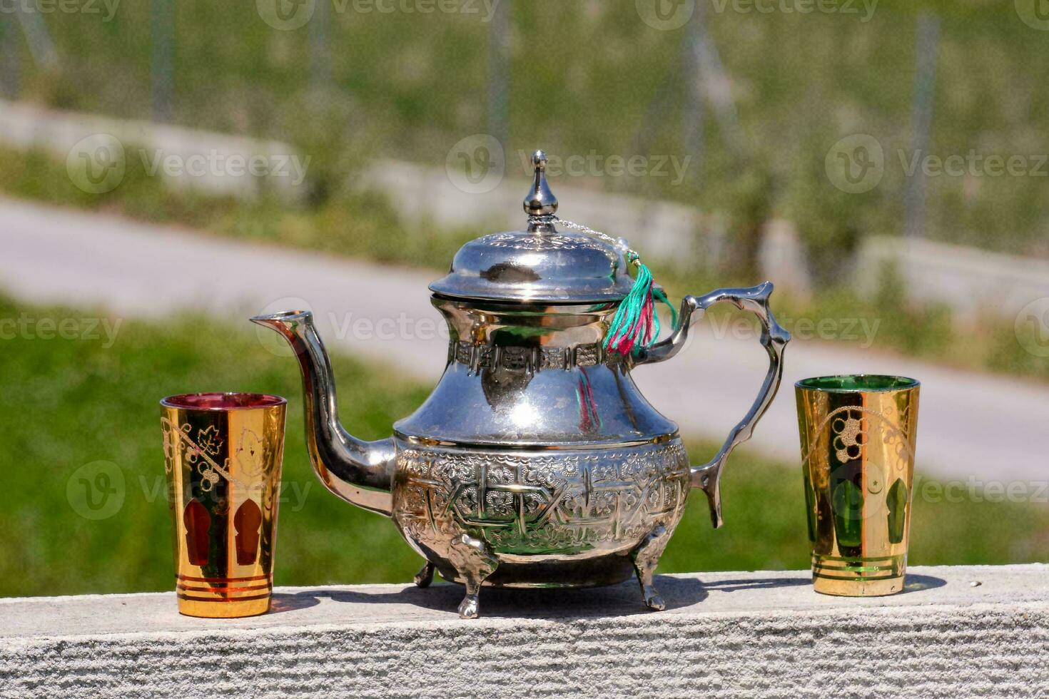 een zilver thee pot en twee kleurrijk cups Aan een richel foto