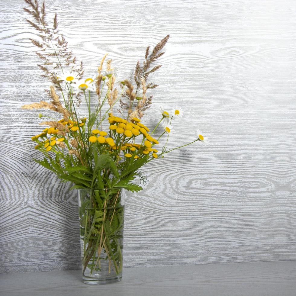 een boeket wilde bloemen in een glazen vaas op een houten tafel foto