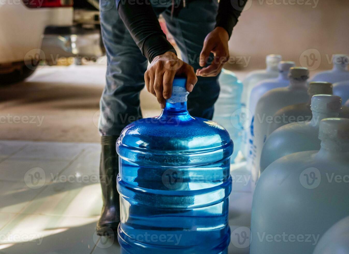 arbeiders optillen drinken water Doorzichtig en schoon in blauw plastic gallon in de terug van een vervoer vrachtauto gezuiverd drinken water binnen de productie lijn naar bereiden voor verkoop.klein bedrijf foto